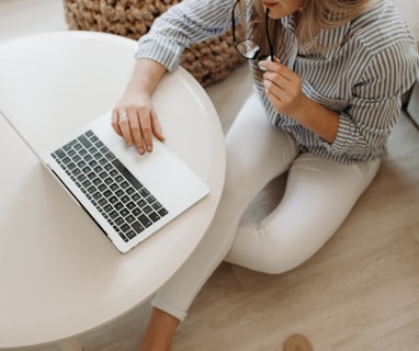 woman in white and black striped dress shirt sitting on floor in front of table while using laptop computer