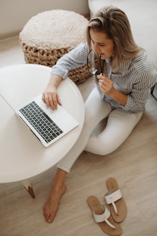 woman in white and black striped dress shirt sitting on floor in front of table while using laptop computer
