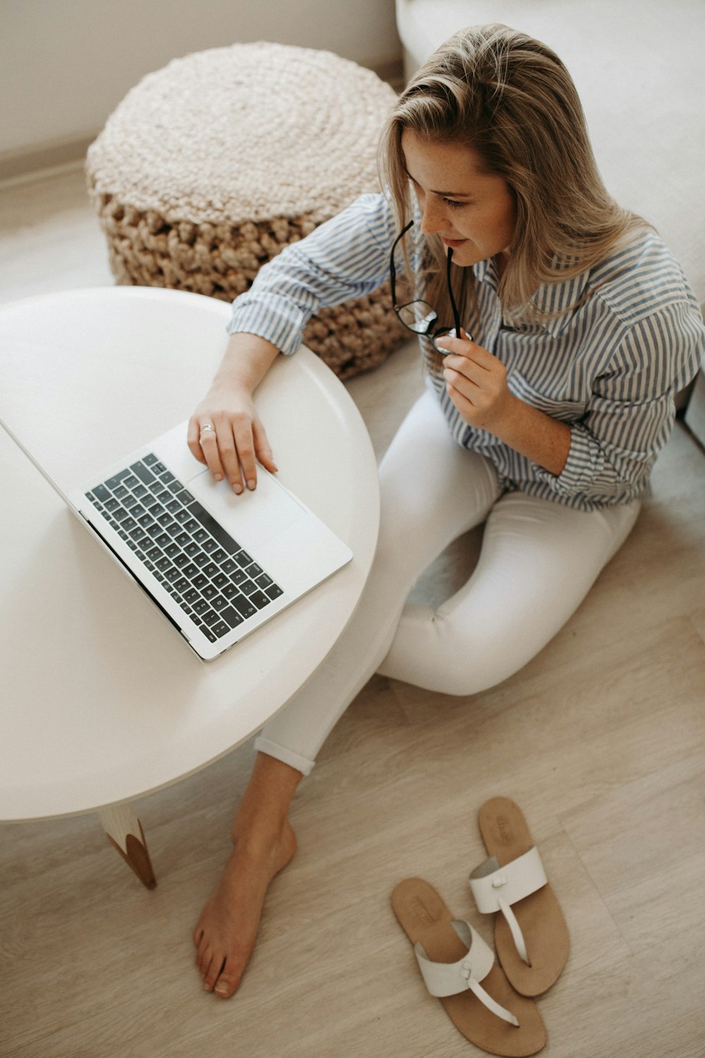 woman in white and black striped dress shirt sitting on floor in front of table while using laptop computer