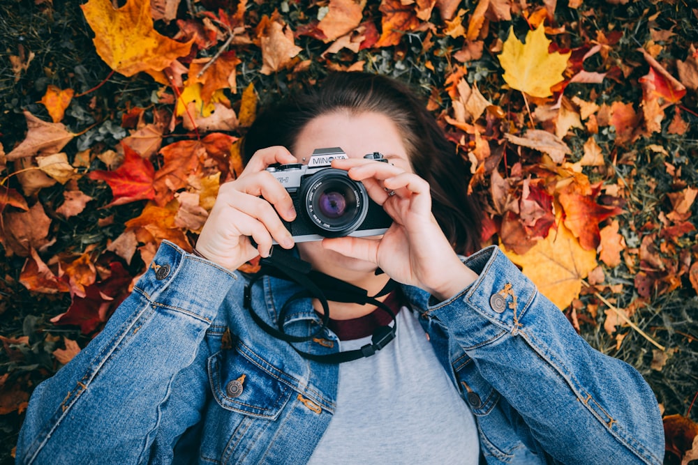 woman laying on maple leaves using black Minolta DSLR camera