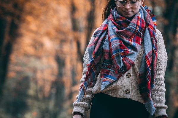 Warm wool scarf wrapped snugly around a person walking through autumn leaves.