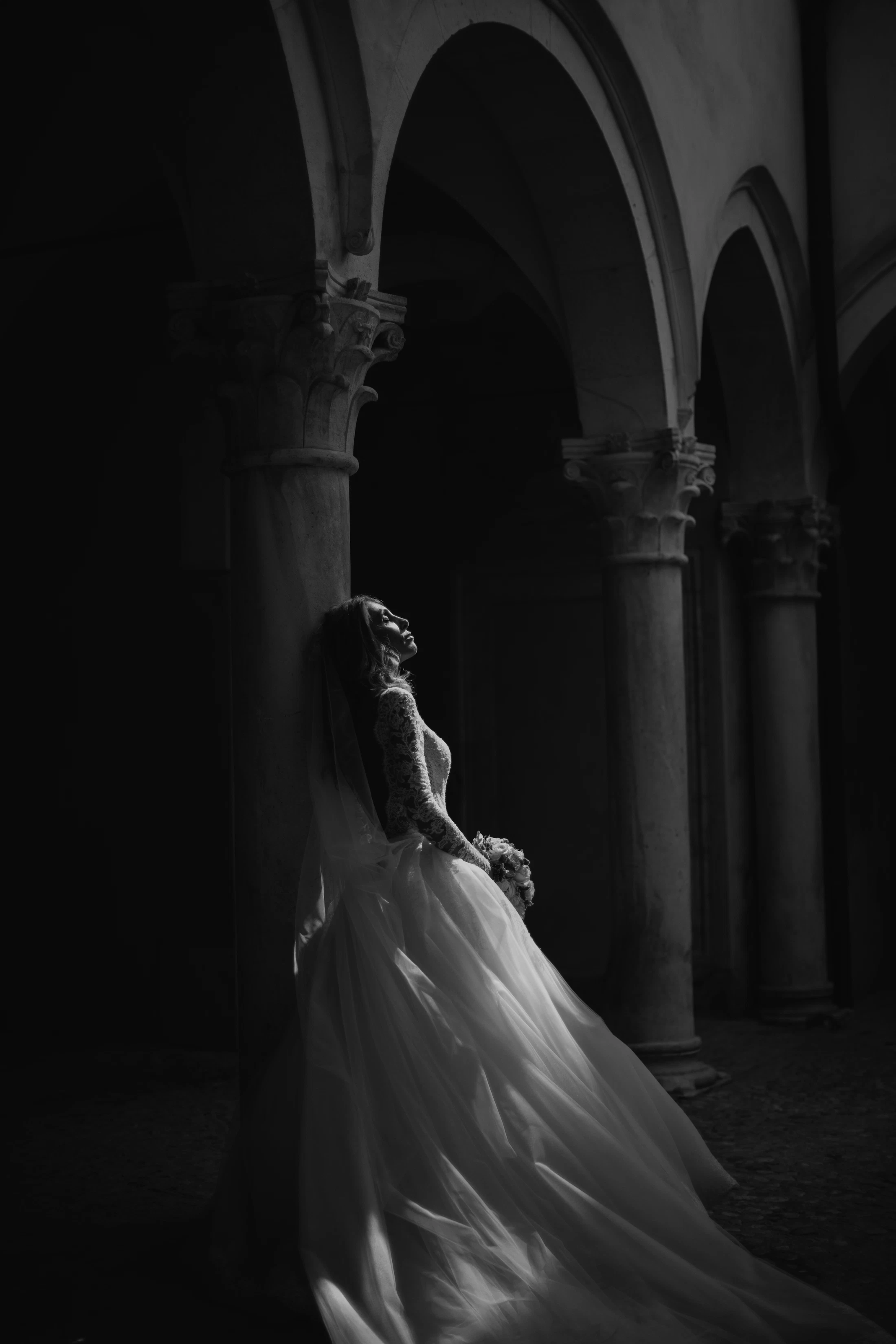 A bride standing between the stone arches of a cloister