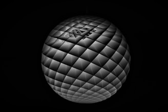 A spherical object with a tessellated pattern of triangular tiles, creating a geometric and futuristic appearance. The pattern is symmetrical, with a reflective quality that emphasizes its three-dimensional shape.