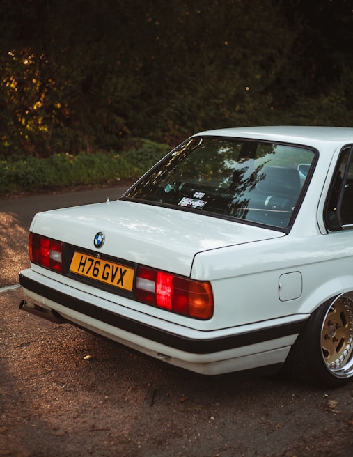 A shiny white BMW 3 Series cruising through the vibrant streets of London with iconic red buses in the background