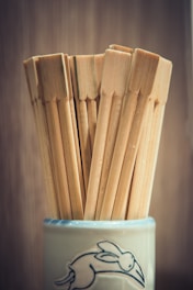 Several wooden chopsticks are neatly arranged in a ceramic cup, which features a line drawing of a rabbit in motion against a blurred background.