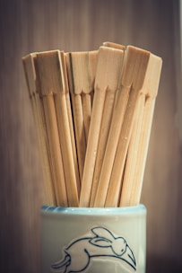 Several wooden chopsticks are neatly arranged in a ceramic cup, which features a line drawing of a rabbit in motion against a blurred background.