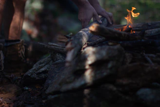 Close-up of rugged hands tying a paracord bracelet beside a campfire.