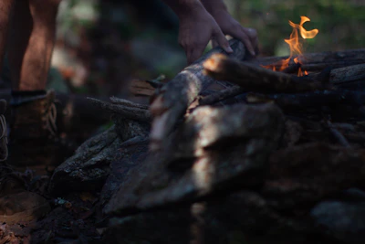 Close-up of rugged hands tying a paracord bracelet beside a campfire.