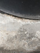 A textured concrete surface with varying shades of grey and patches of discoloration due to wear or moisture. The upper section includes a darker, curved area, suggesting a tire or similar object pressing against the concrete.