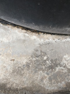 A textured concrete surface with varying shades of grey and patches of discoloration due to wear or moisture. The upper section includes a darker, curved area, suggesting a tire or similar object pressing against the concrete.