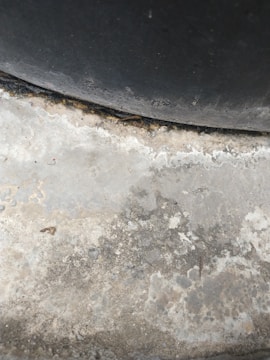 A textured concrete surface with varying shades of grey and patches of discoloration due to wear or moisture. The upper section includes a darker, curved area, suggesting a tire or similar object pressing against the concrete.