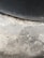 A textured concrete surface with varying shades of grey and patches of discoloration due to wear or moisture. The upper section includes a darker, curved area, suggesting a tire or similar object pressing against the concrete.