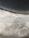 A textured concrete surface with varying shades of grey and patches of discoloration due to wear or moisture. The upper section includes a darker, curved area, suggesting a tire or similar object pressing against the concrete.
