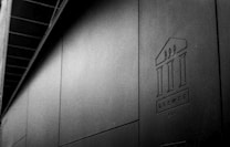 A black and white image featuring a minimalist architectural design with a prominent logo that resembles a stylized building or columns. The logo has the word 'DEEWE' along with a number '001' below it. The composition is sleek and modern, with a clean and textured surface.