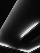 A modern ceiling design with recessed lighting, featuring sharp geometric lines and contrasting areas of light and shadow. The interplay of light appears to highlight the architectural elements, giving a minimalist and contemporary feel.