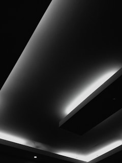 A modern ceiling design with recessed lighting, featuring sharp geometric lines and contrasting areas of light and shadow. The interplay of light appears to highlight the architectural elements, giving a minimalist and contemporary feel.