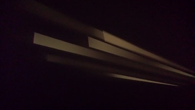Several parallel beams of light are projected diagonally across a dark background, creating an abstract and mysterious effect.