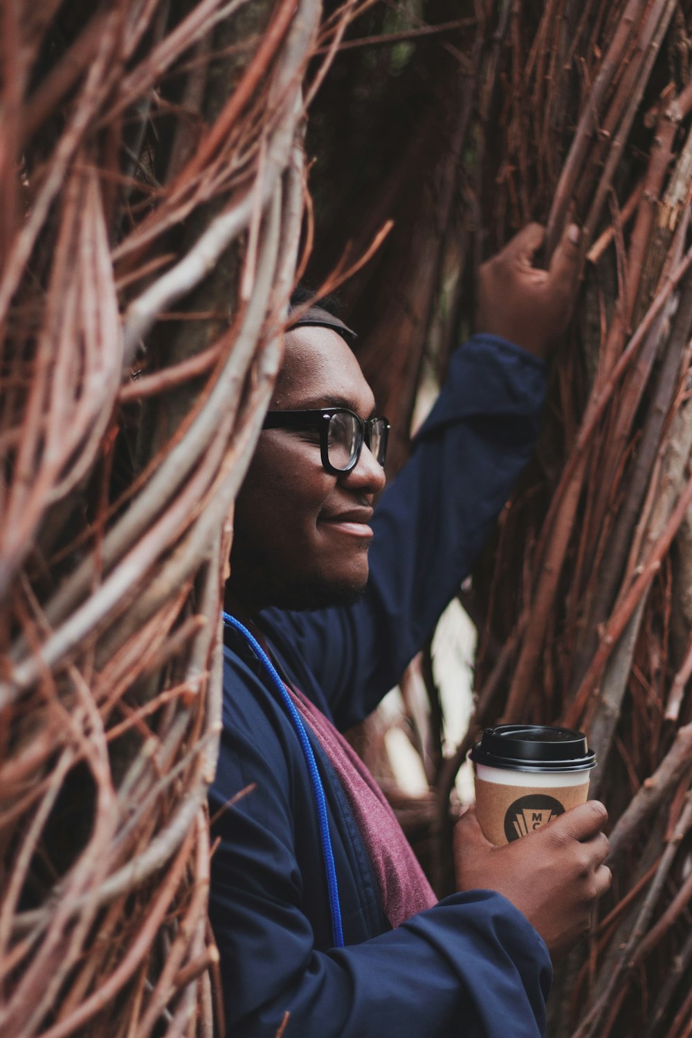 smiling man standing beside woods while holding travel mug during daytime