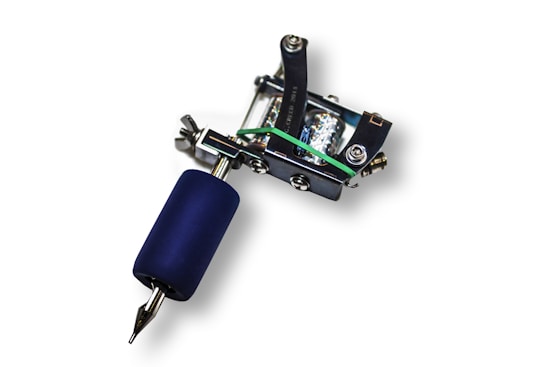 A tattoo machine featuring a metal frame and blue grip with various screws and a needle protruding from one end, placed against a white background.