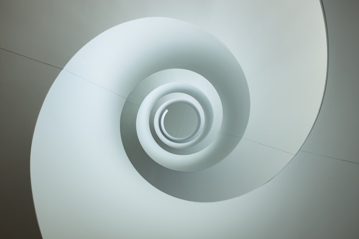 Looking up through the centre of a white and grey spiral staircase, an abstract stand-in for the spiral imagery Spiralism is named for
