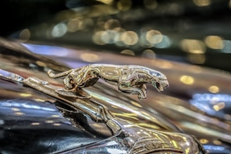 A shiny metallic jaguar hood ornament mounted on a classic car, with a background of softly blurred bokeh lights creating a luxurious and elegant atmosphere.