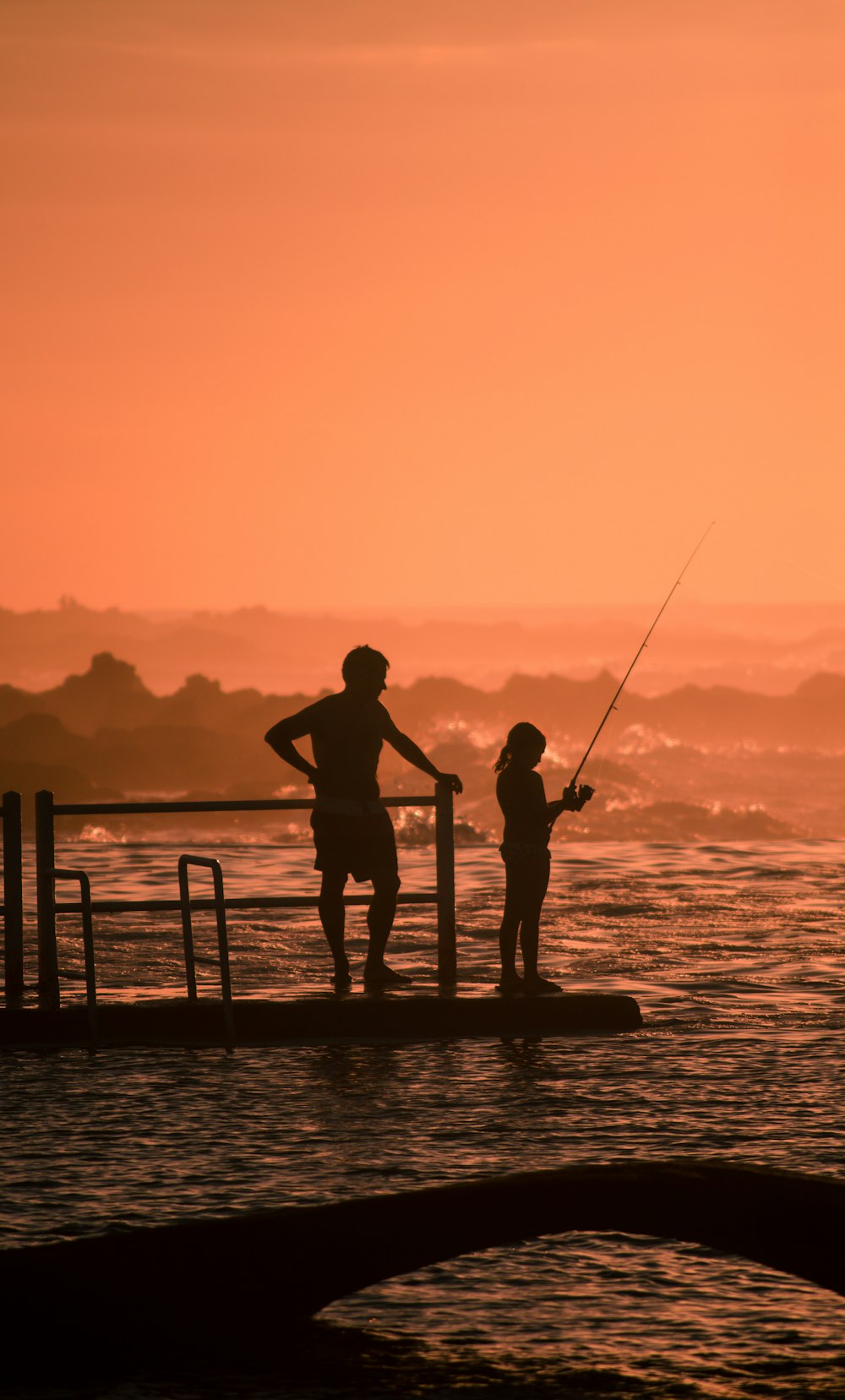 silhouette of man and girl fishing during sunset