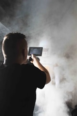 A cameraman is filming a person in sports gear, specifically football equipment, amid dense, theatrical smoke.