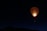A colorful hot air balloon illuminated from within, floating against a dark night sky. The balloon's vibrant pattern contrasts with the deep blue and black background, creating an eye-catching scene. Below the balloon, the silhouette of a landscape is faintly visible.