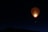 A colorful hot air balloon illuminated from within, floating against a dark night sky. The balloon's vibrant pattern contrasts with the deep blue and black background, creating an eye-catching scene. Below the balloon, the silhouette of a landscape is faintly visible.
