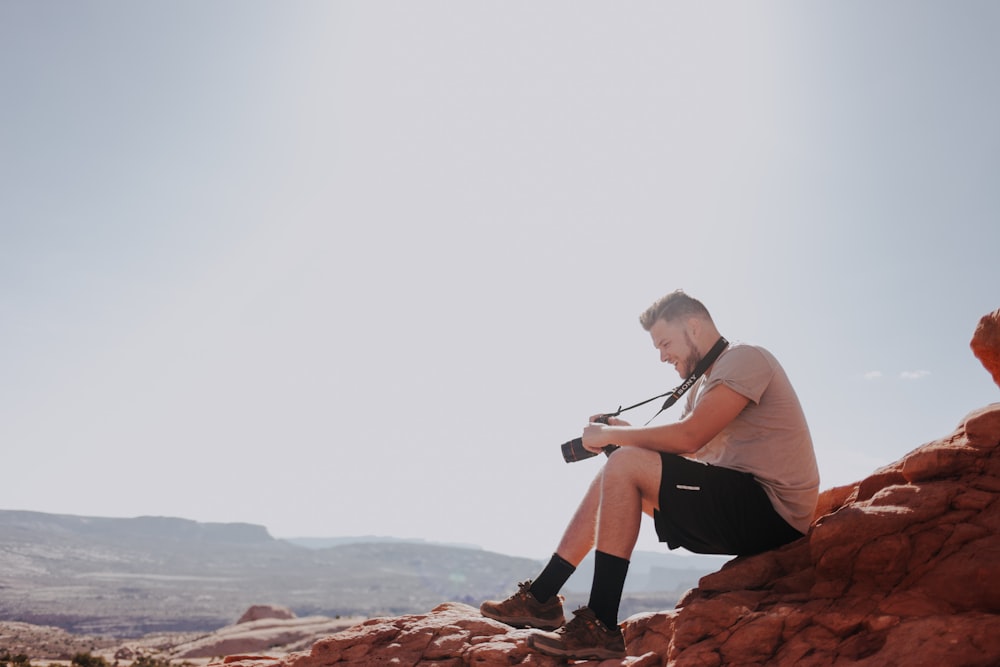 man sitting on rock formation holding camera