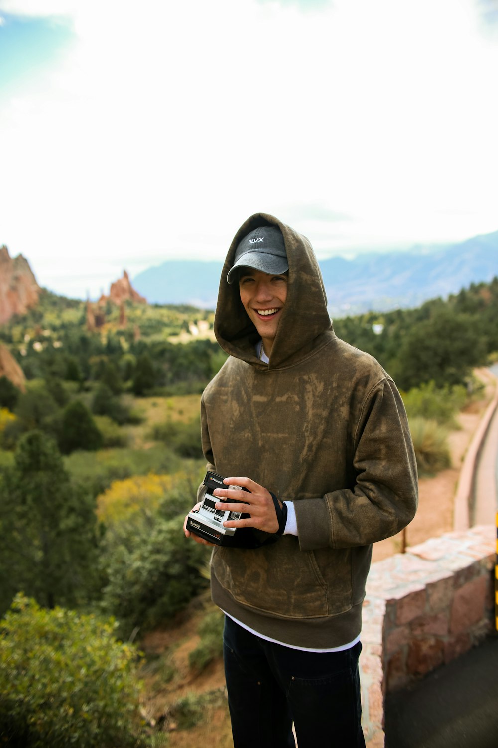 smiling man holding camera standing on cliff during daytime