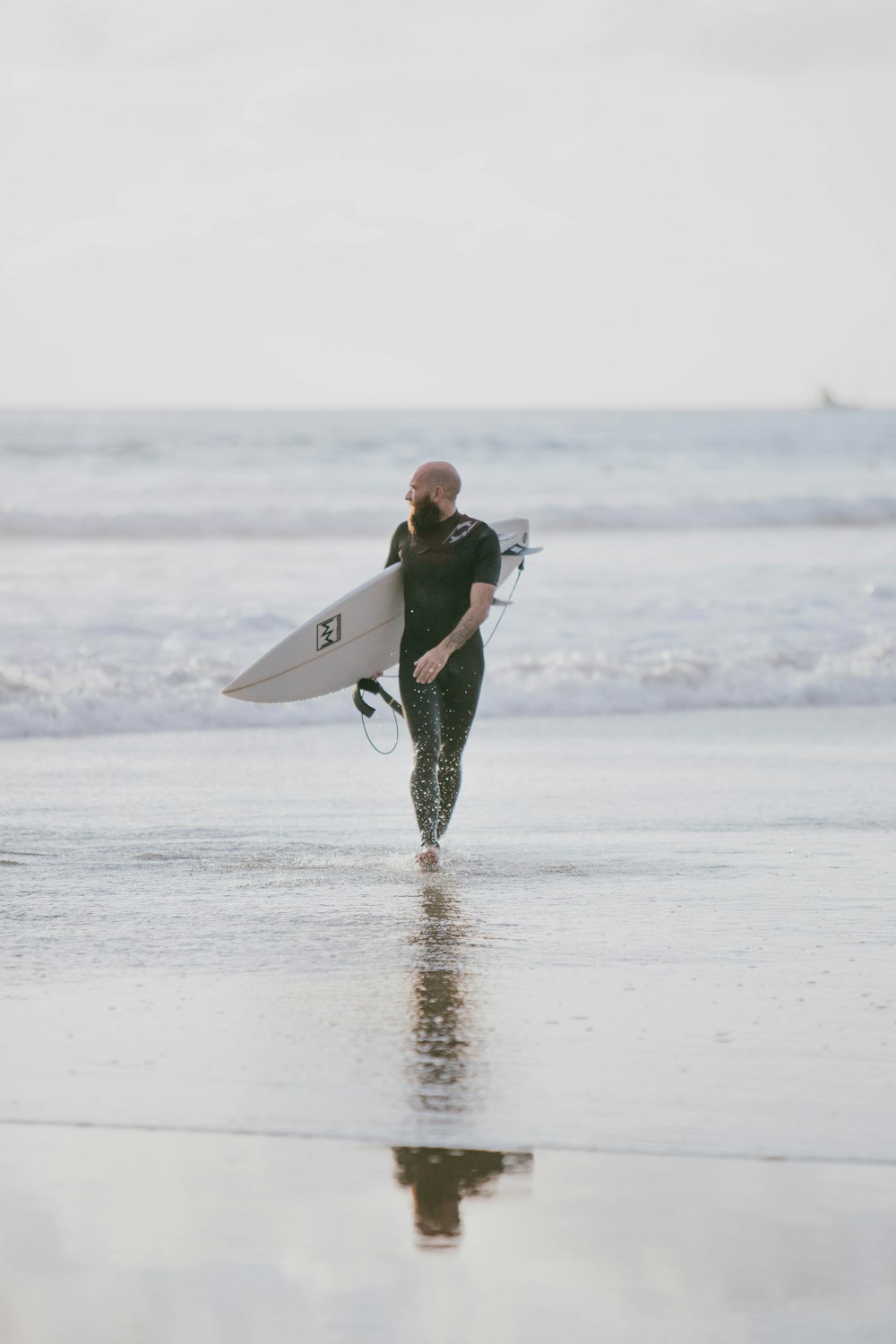 man walking on shore holding white surfboard