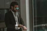 Groom adjusting his cufflinks in a sleek, modern suit by a large window.