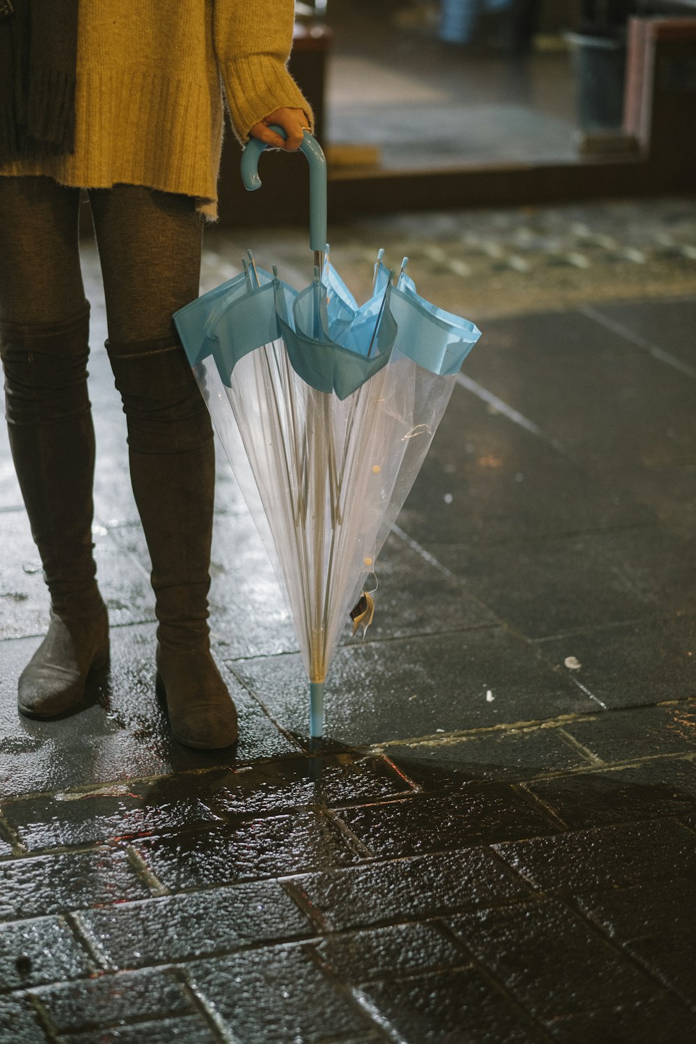 person in grey sweater and brown thigh-high boots holding umbrella