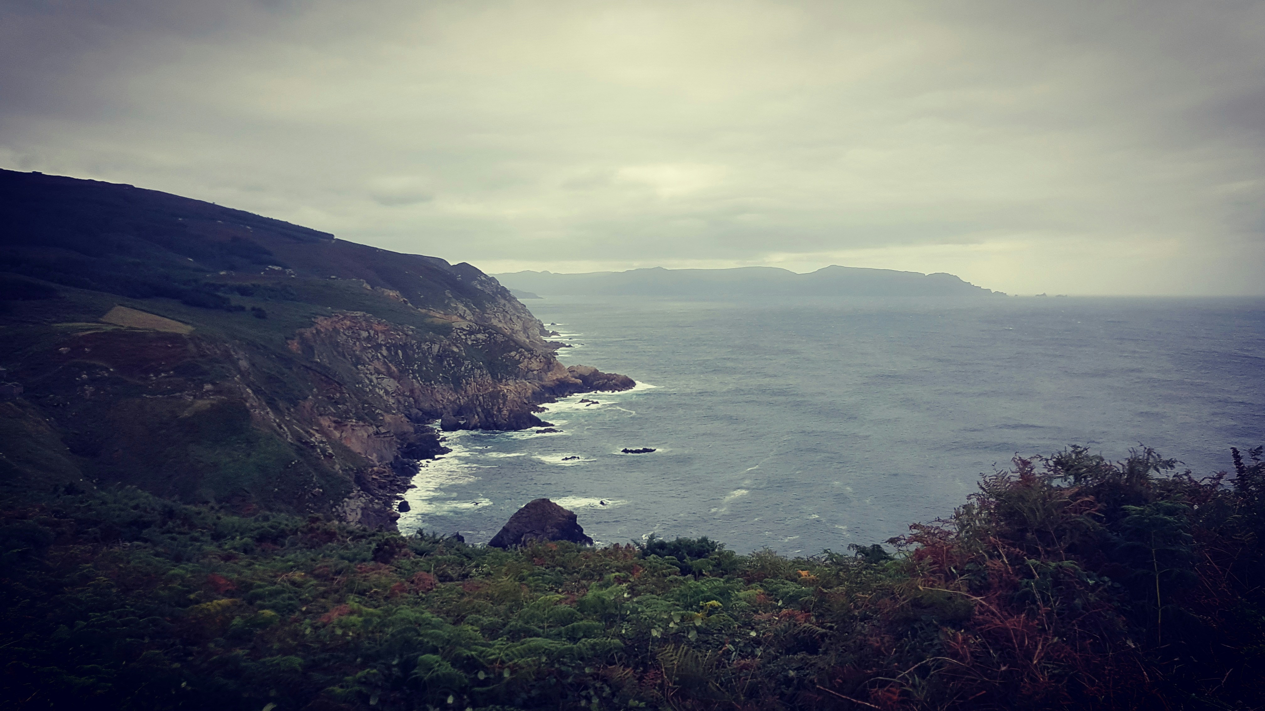 Remote Faroe Islands coastline, dramatic sea cliffs, dark ocean, atmospheric overcast, wild remoteness