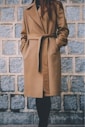 woman wearing brown single-breasted coat standing in front of gray brick wall