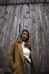 smiling woman in brown coat by wooden panel