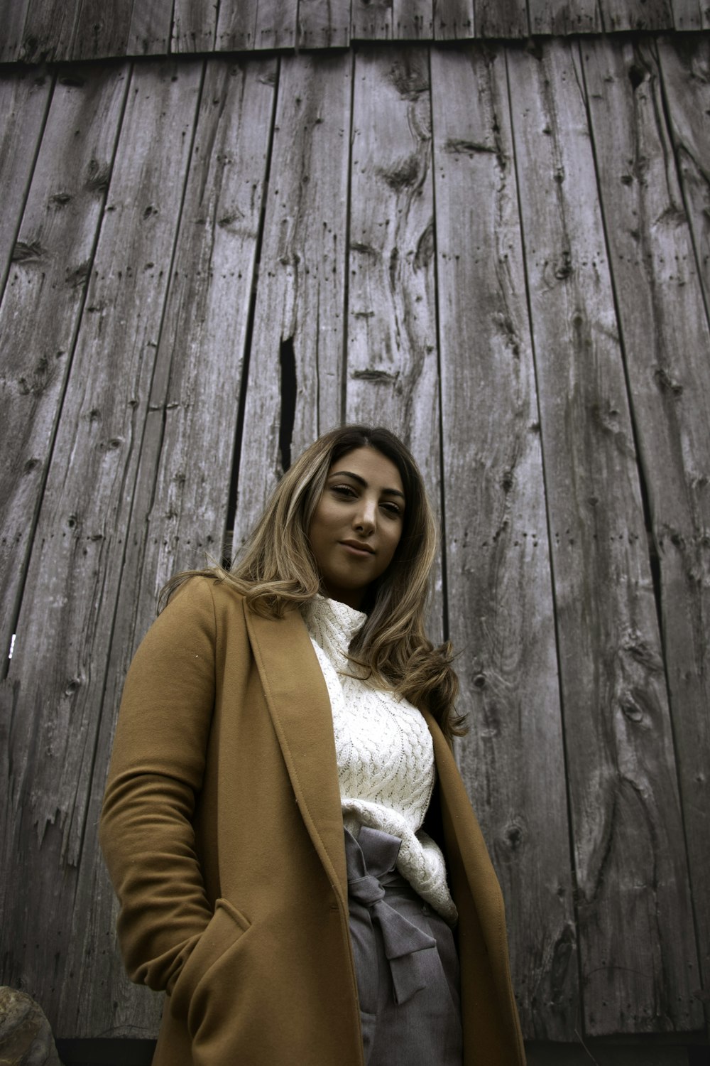 smiling woman in brown coat by wooden panel