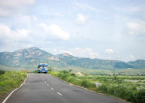 A rural minibus navigating a scenic mountain road surrounded by lush green trees.