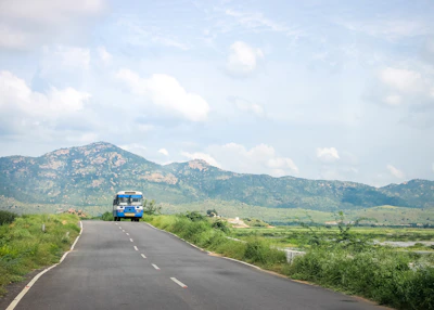 A rural minibus navigating a scenic mountain road surrounded by lush green trees.