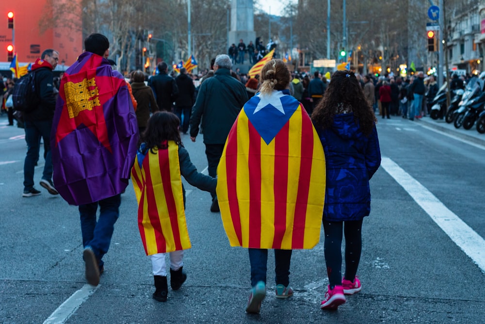 Cuatro personas que caminan por el camino con capas de bandera