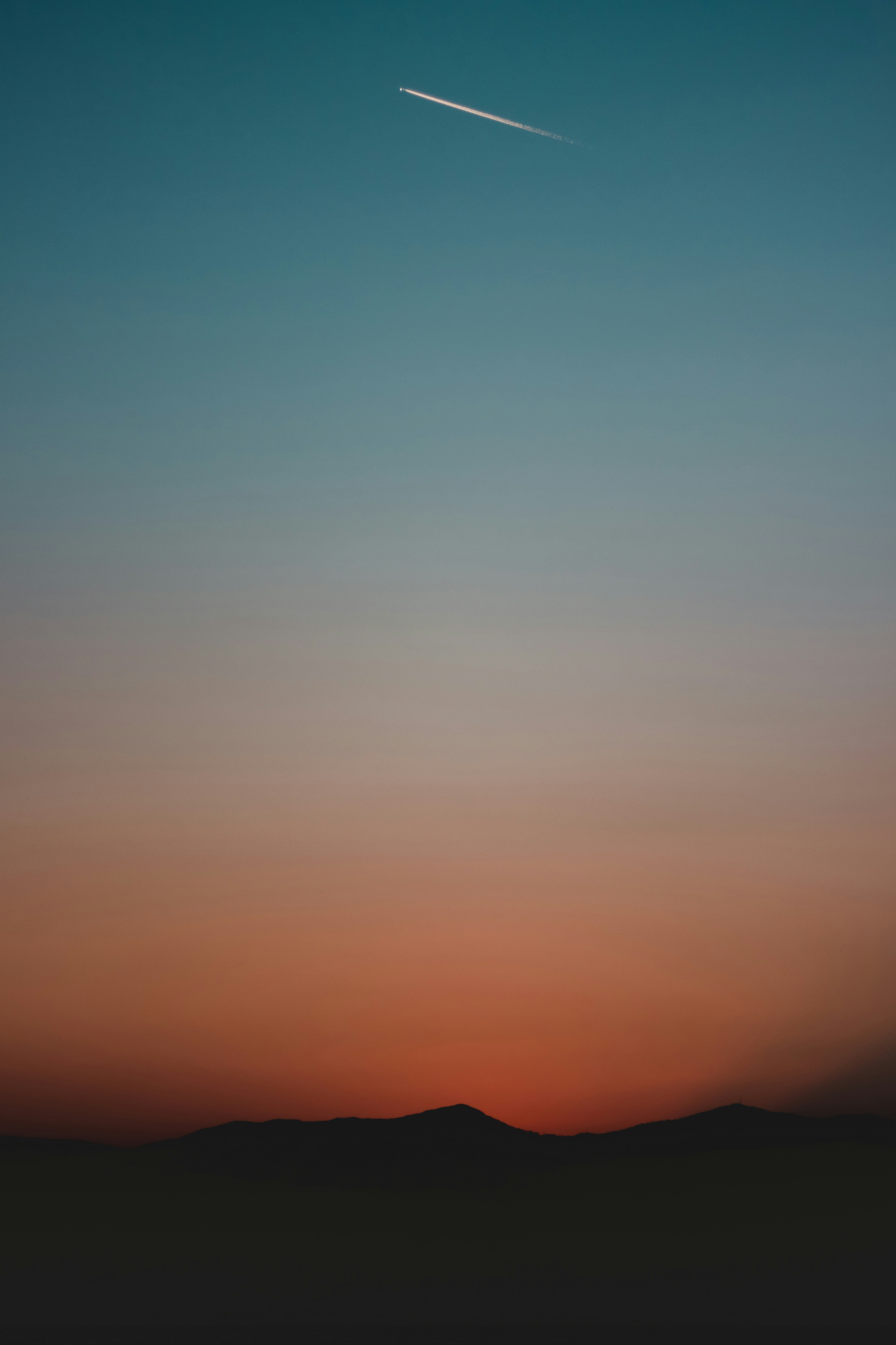 silhouette of mountain under golden hour with contrail