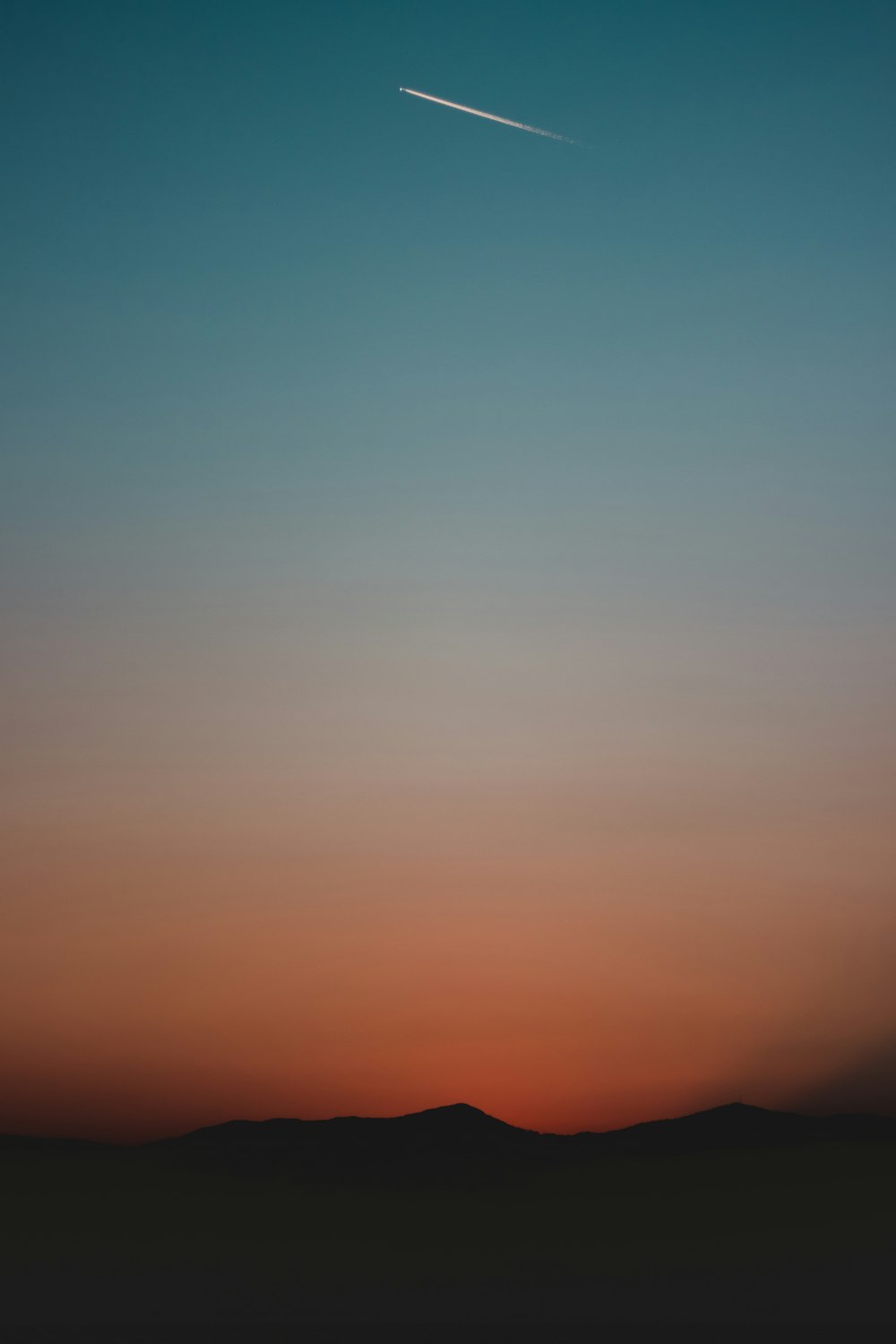 silhouette of mountain under golden hour with contrail