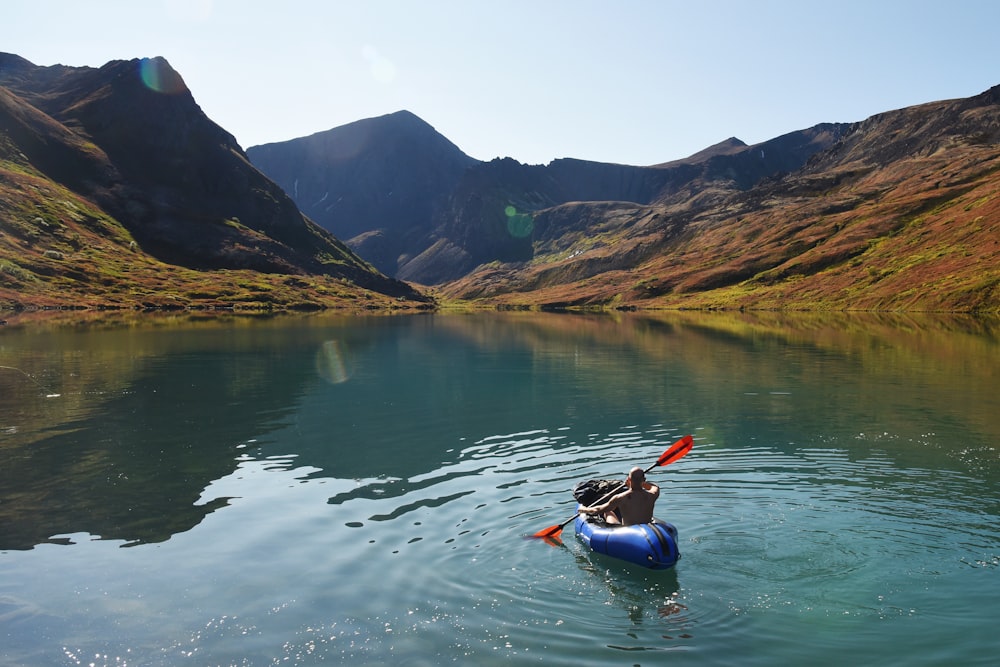 man riding on kayak surrounded by mountains