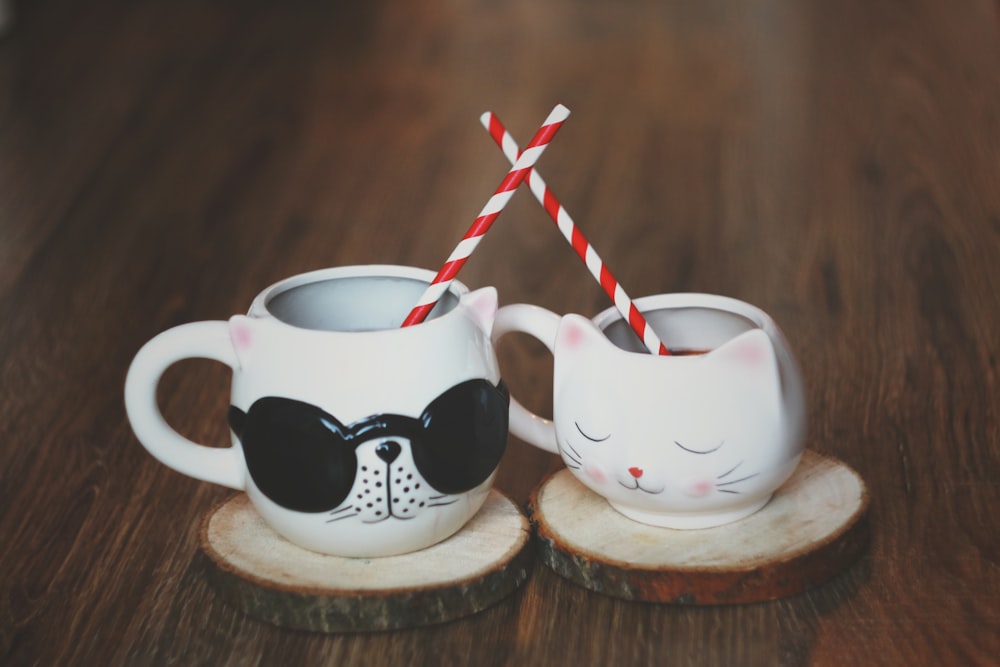 two ceramic cat shaped cups with wood slice coasters and with straws