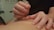 A person is performing acupuncture by gently inserting a thin needle into another person's skin. The focus is on the hands and needle, with a tattoo visible on the forearm. The setting appears to be a clinical environment with diagrams on the wall.