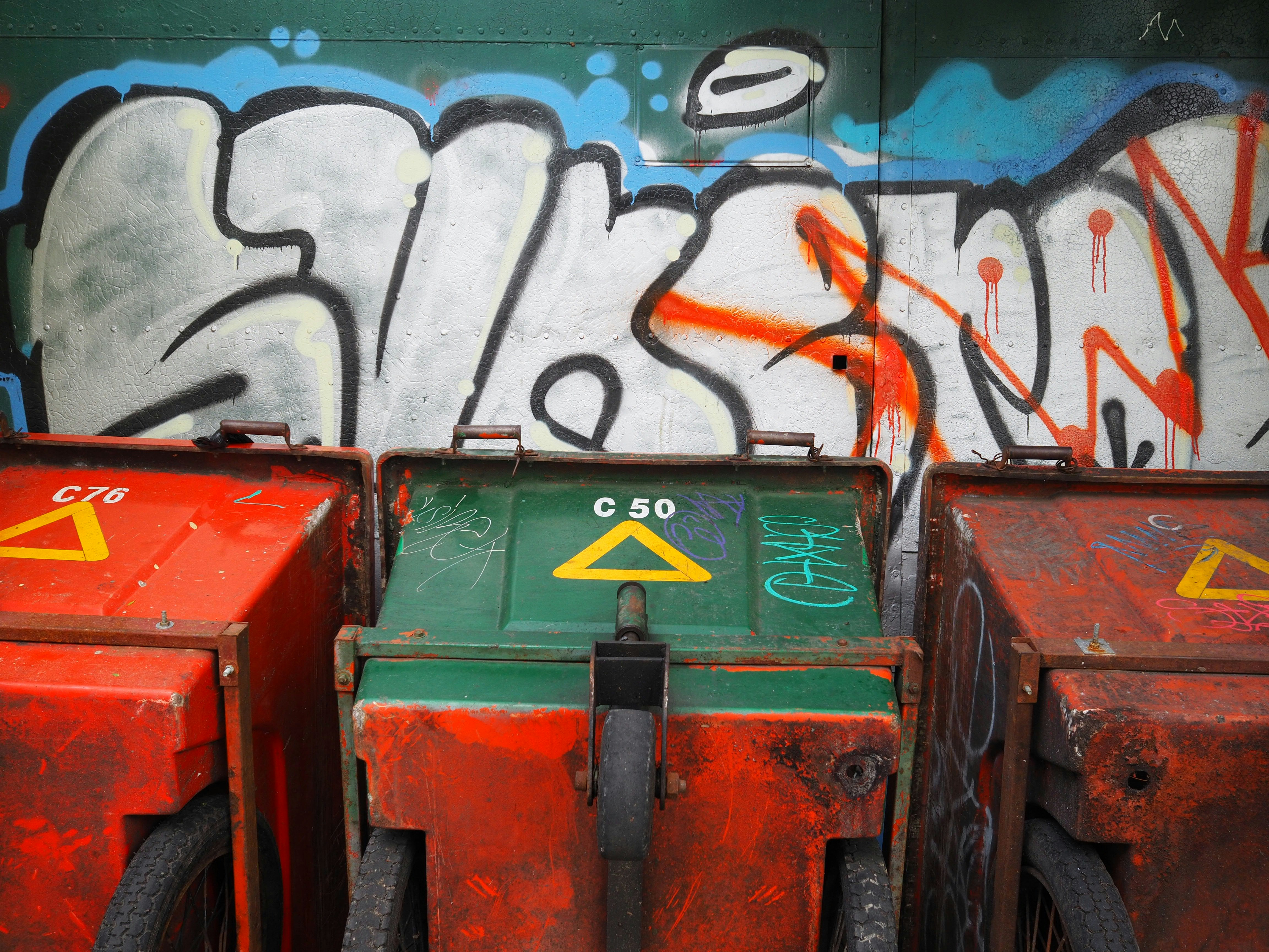 three red and green containers beside graffiti wall