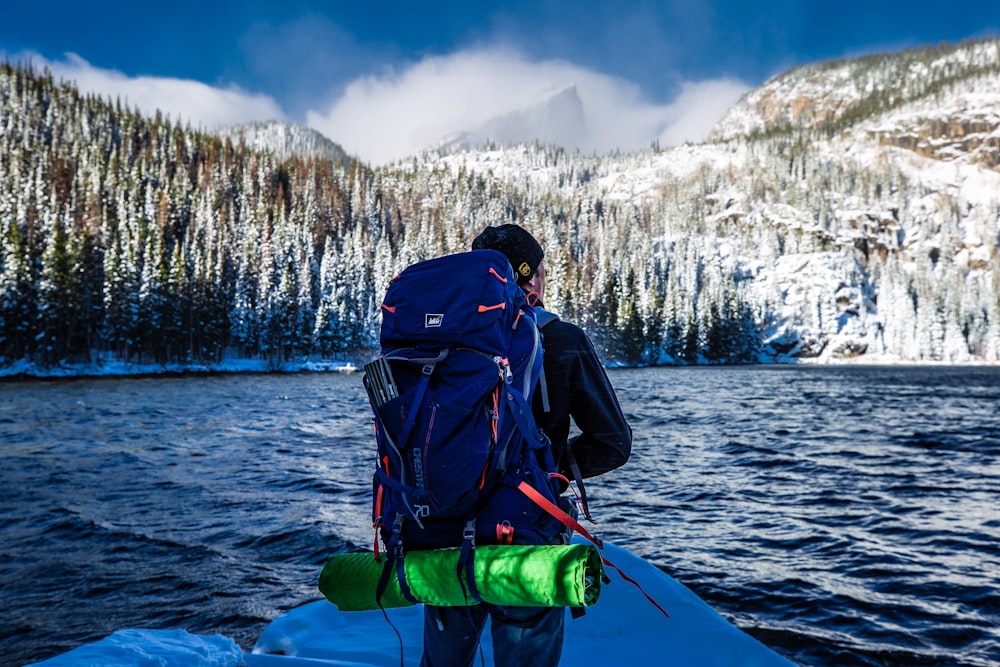 man standing with blue hiking bag front of lake