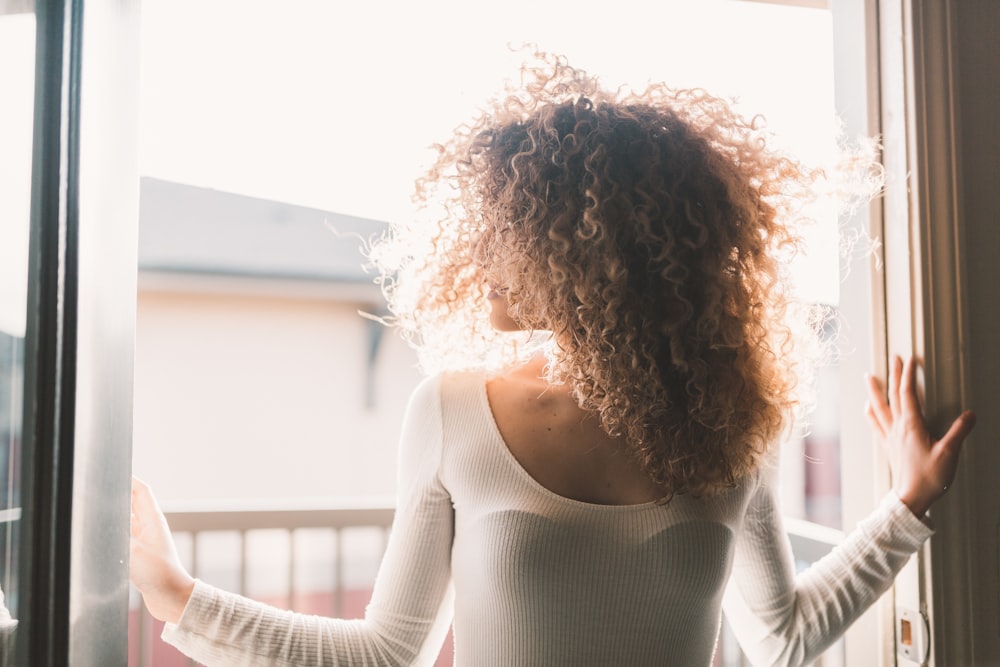 woman wearing white long-sleeved shirt standing beside sliding-door