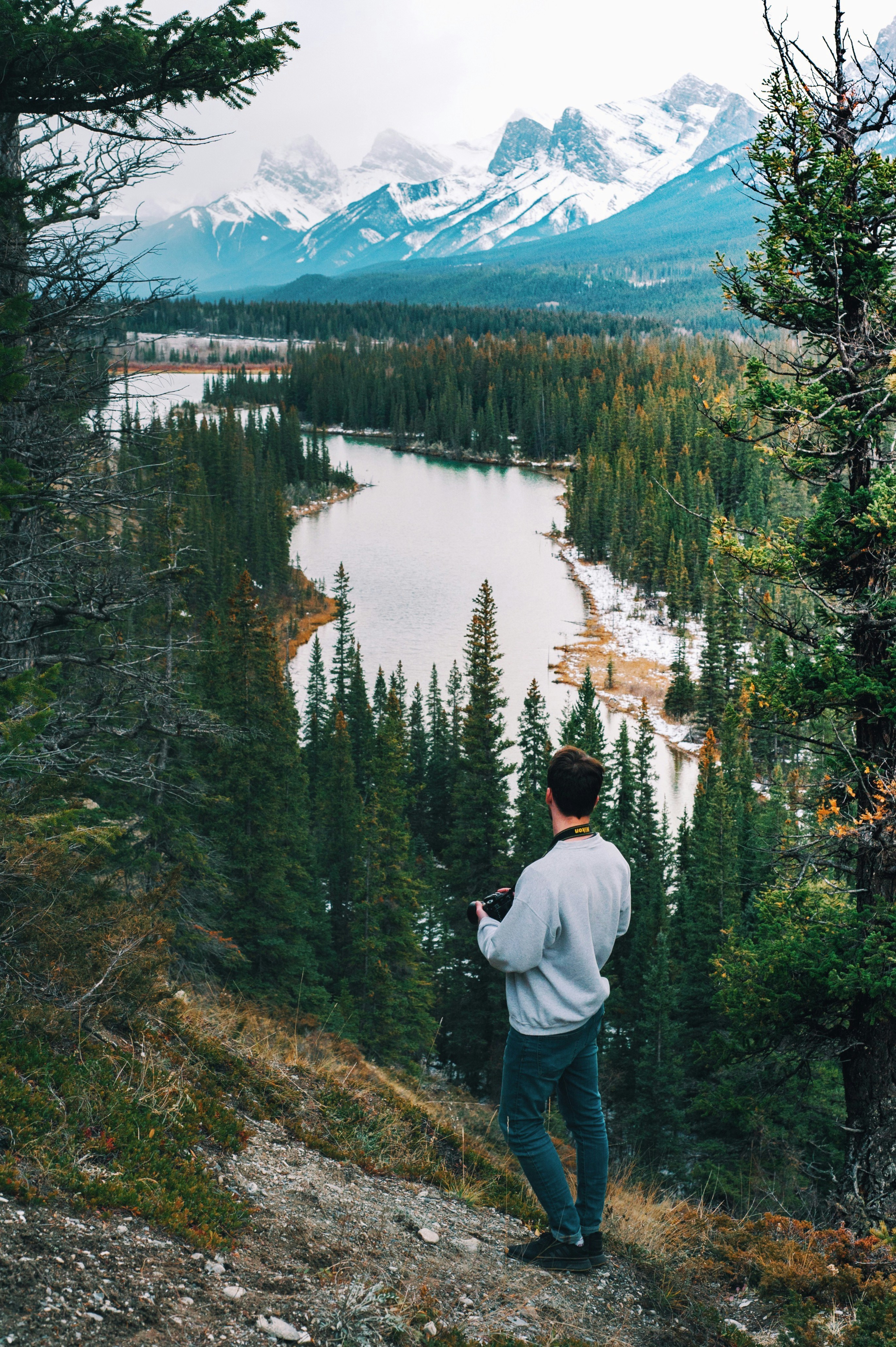 man wearing sweater standing on cliff watching river